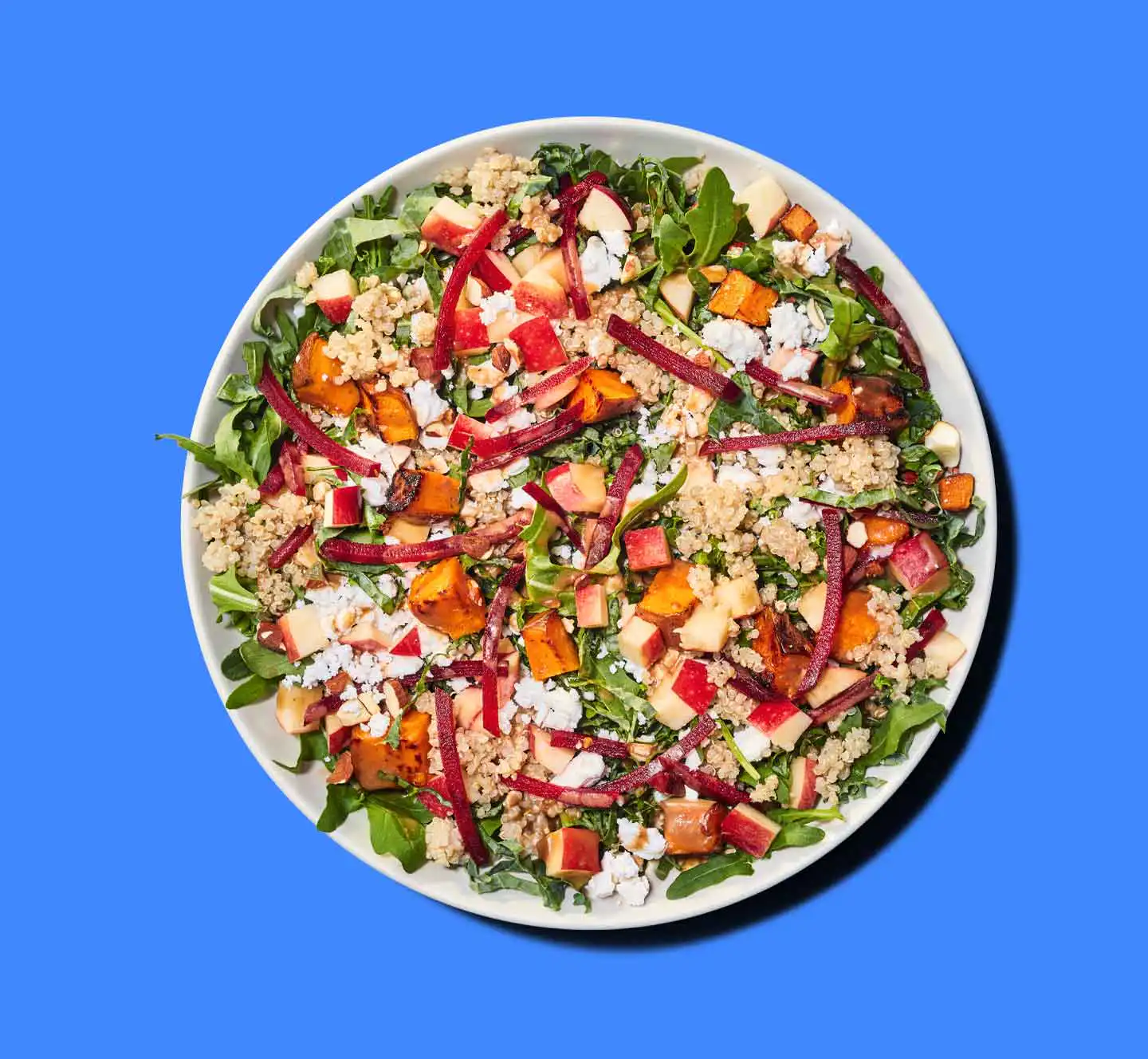 Overhead view of a salad with greens, quinoa, apples, beets, and roasted sweet potato on a blue background