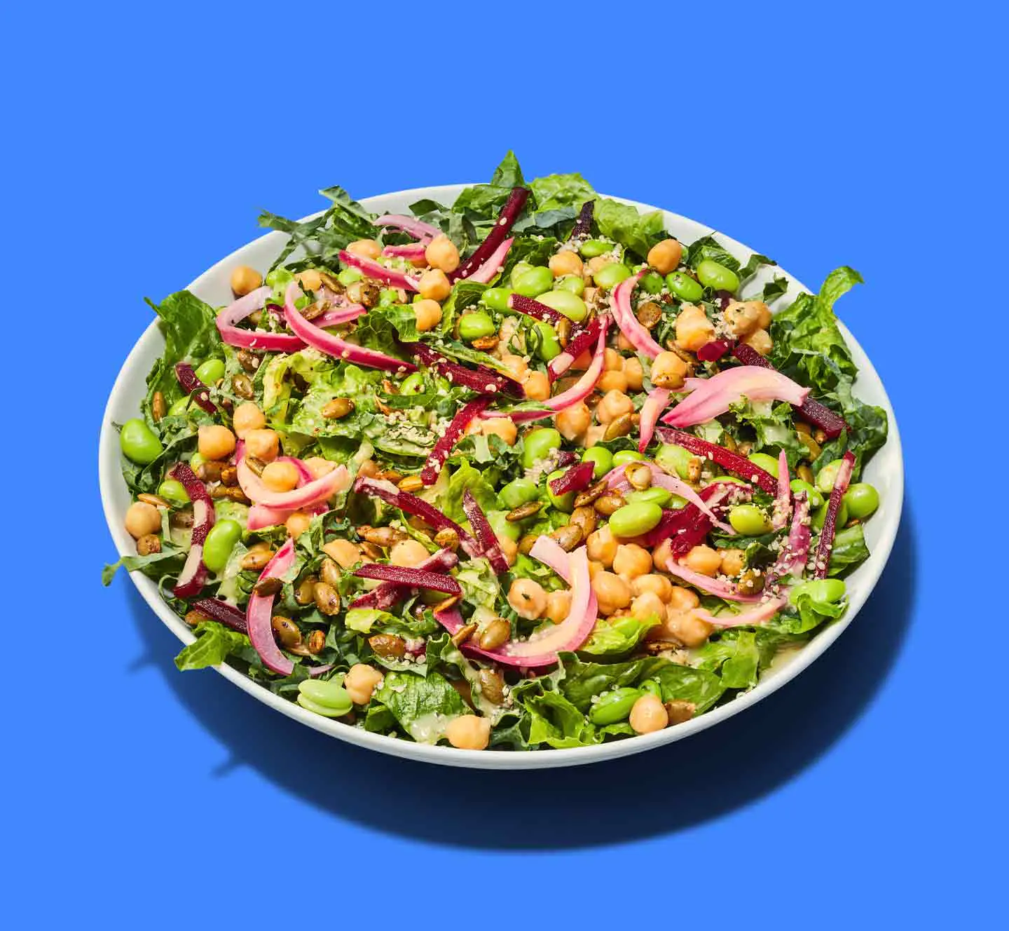 A salad with chickpeas, edamame, pickled onions, beets, and greens on a blue background